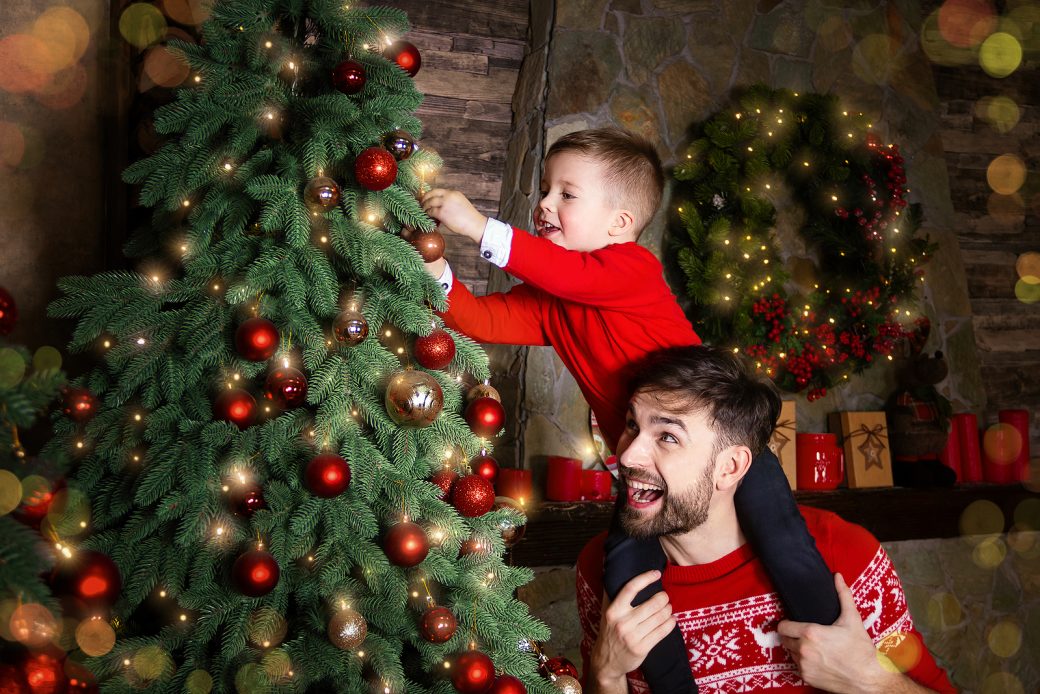 Happy Father and son enjoying decorating Christmas tree with Christmas balls and light garland preparing for celebrating winter holidays: Merry Christmas Eve and Happy New Year 2019. Family concept.