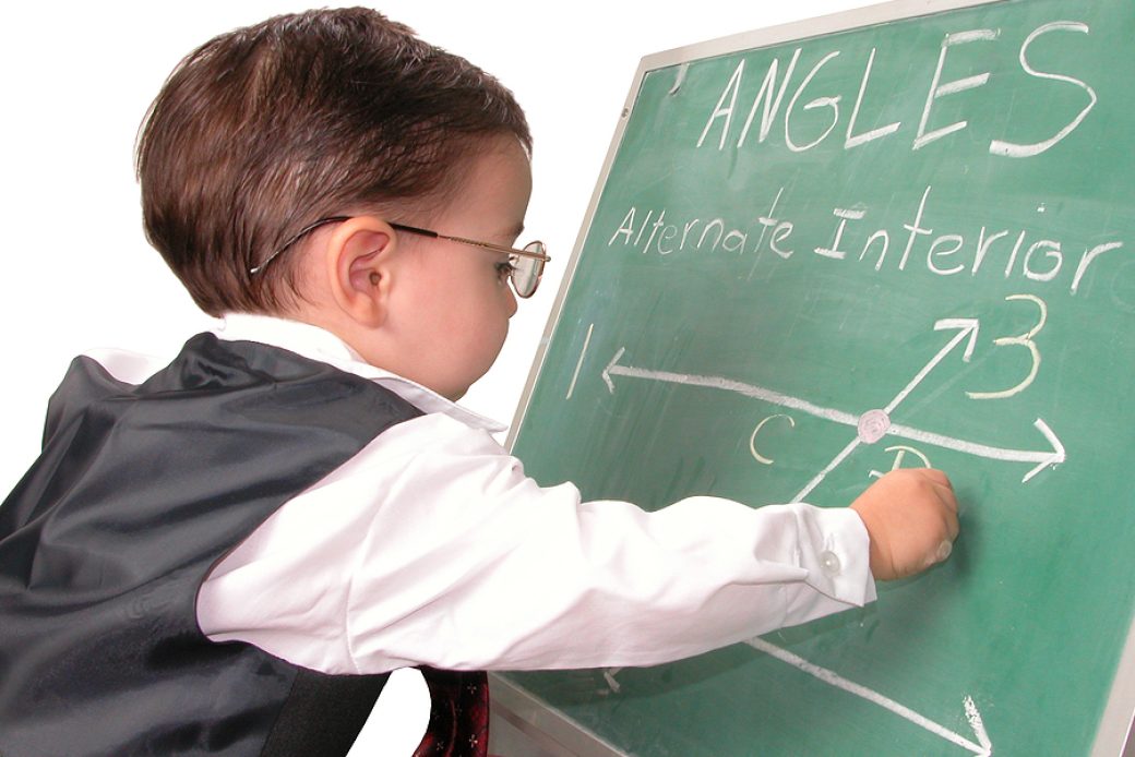 Adorable child prodigy at chalkboard doing math equations for school.  Dressed in suit with glasses.