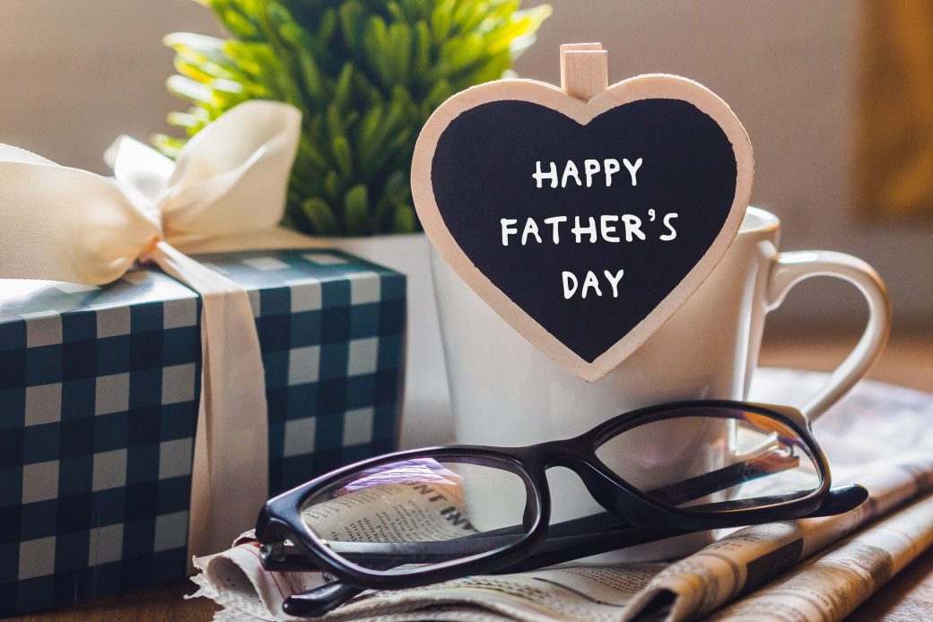 Happy fathers day concept. coffee cup with gift box, heart tag with Happy father's day text and newspaper, glasses on wooden table background.