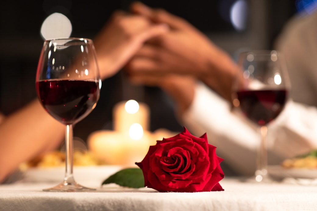 Romantic Date. Red Rose Lying On Table, Loving Afro Couple Holding Hands During Valentines Dinner In Restaurant. Selective Focus